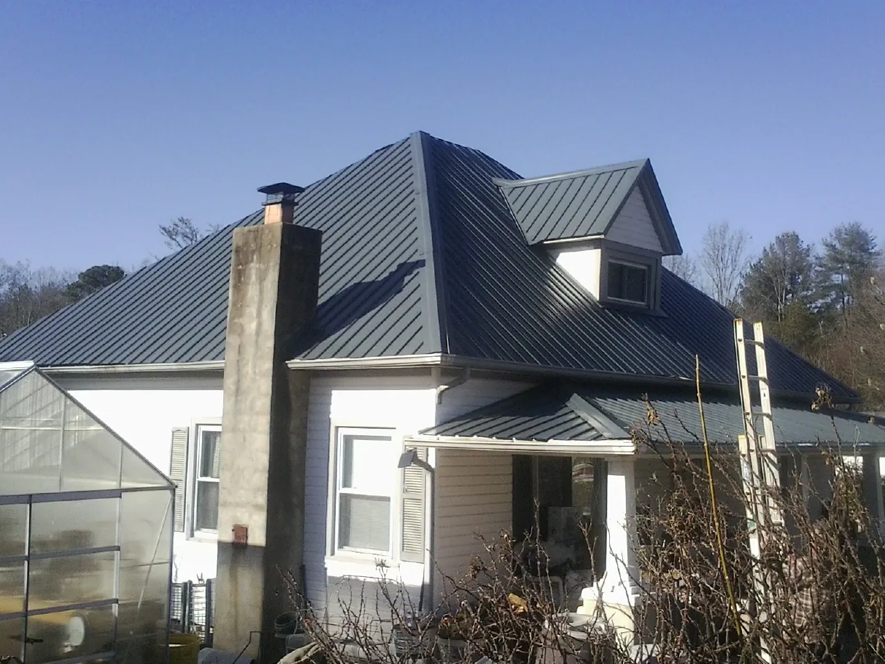 Dark blue standing seam metal roof on a white farmhouse with dormer — Slate & Tile Roof Repair by Roofing Brothers in Brasstown