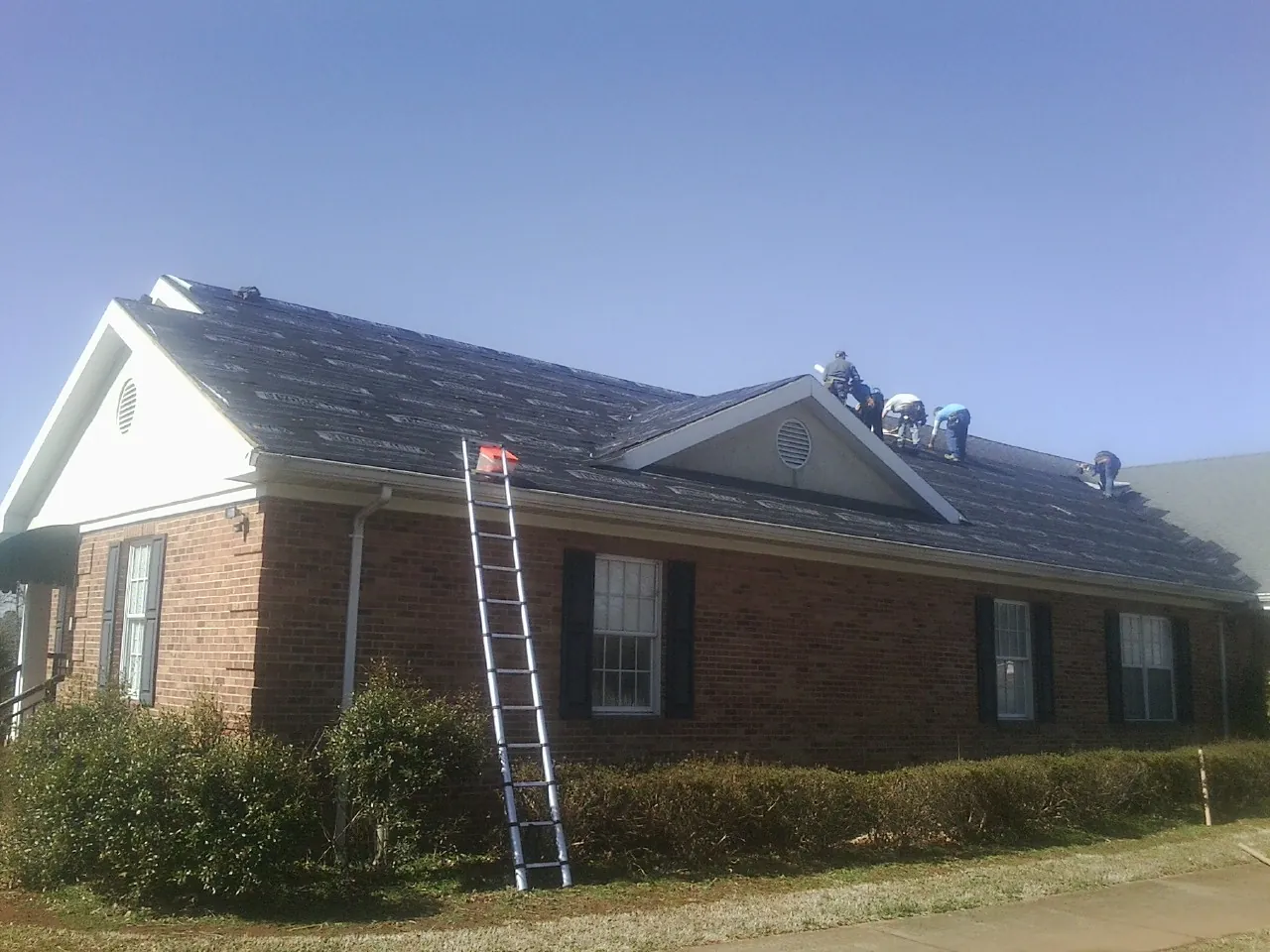 Crew tearing shingles off a brick ranch roof with a ladder set — Emergency Roof Repair work by our crew in Brasstown