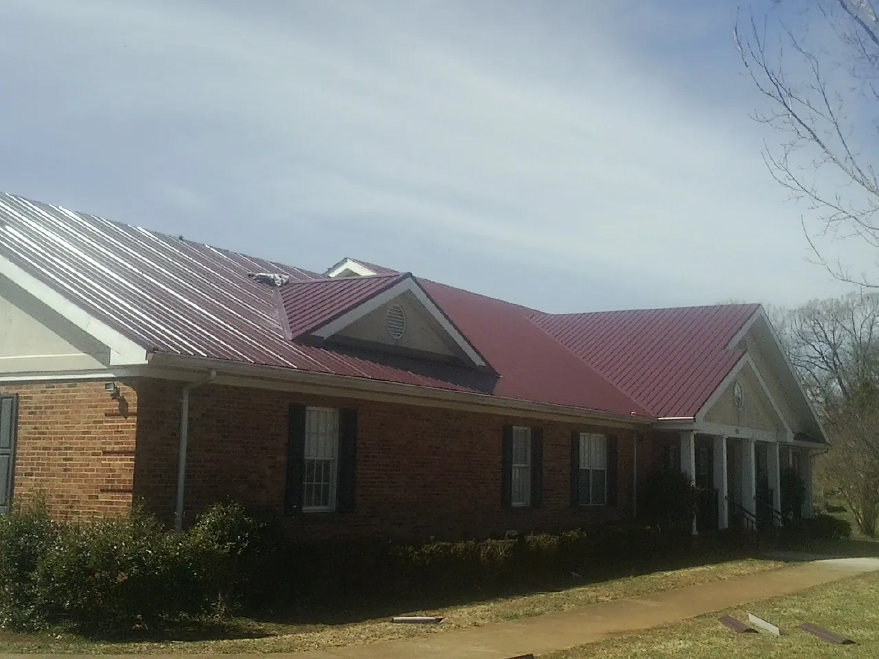 Red metal roof with gabled entries on a long brick building, from a Hail Damage Roof Repair job in Brasstown