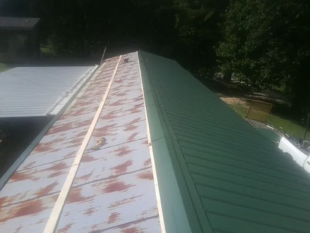 Old rusted panels beside newly installed green metal roofing — Wind Damage Roof Repair by Roofing Brothers in Brasstown