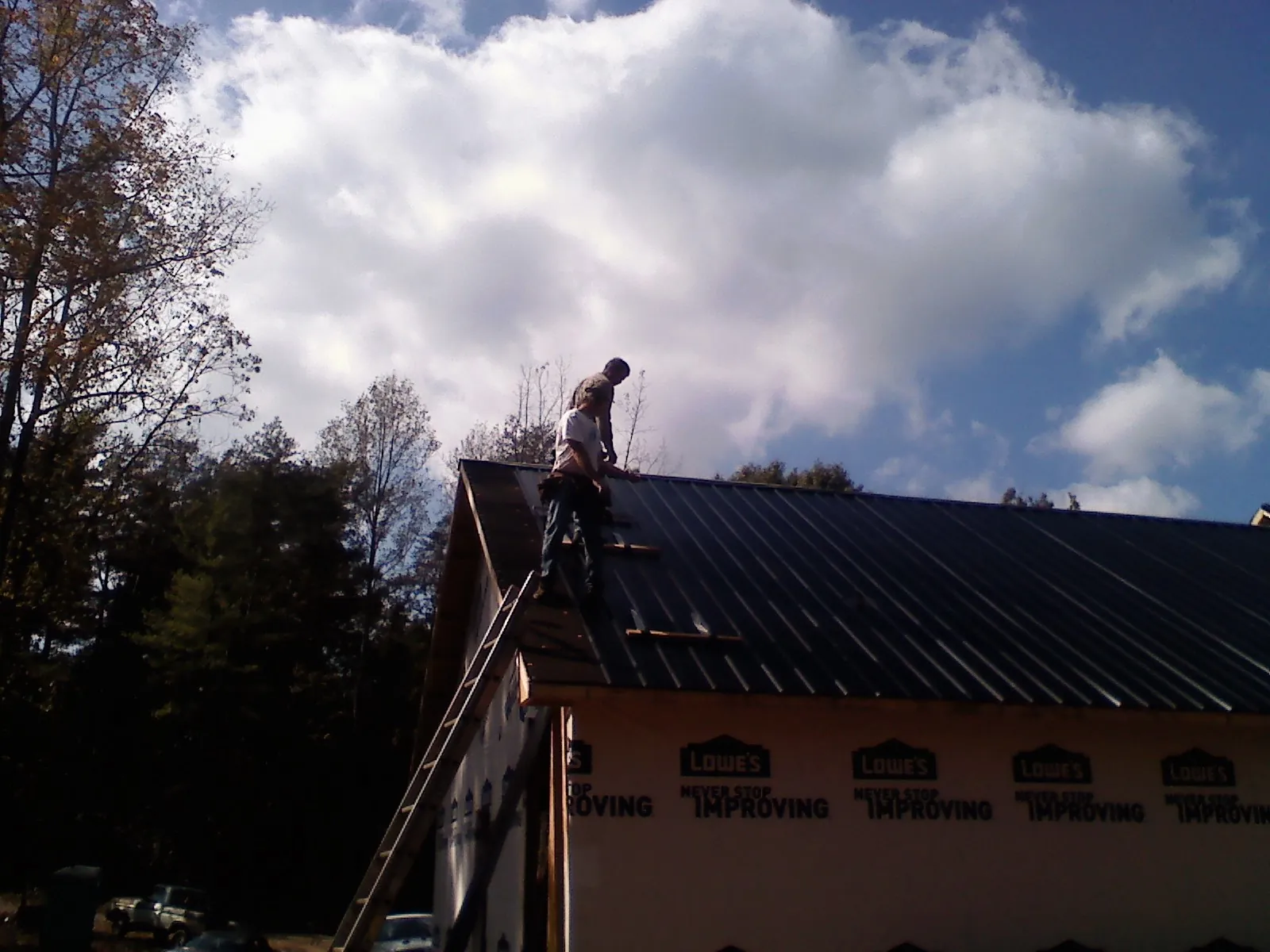 Roofer fastening dark metal panels high against a cloudy sky, from a Roof Inspection job in Brasstown