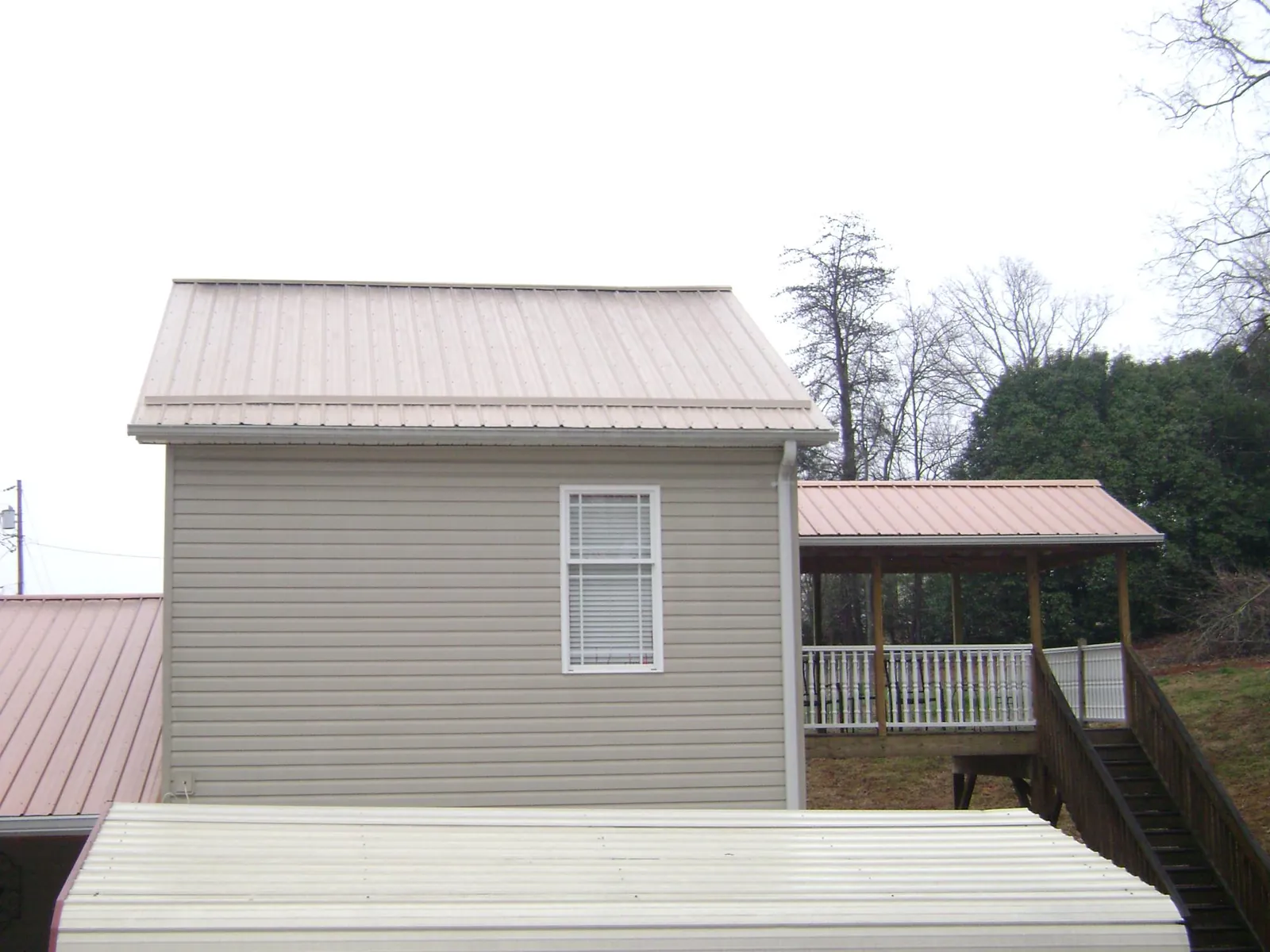 Tan metal roofs on a two story addition and attached porch, from a Roof Replacement job in Brasstown